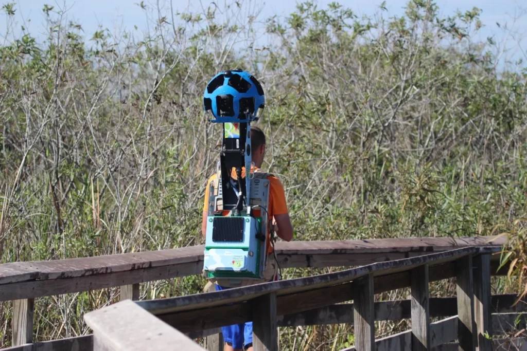 A Google Street View Trekker camera backpack being carried along a wooden boardwalk, the kind of camera used for landmark-only coverage